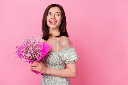Photo of adorable thoughtful lady wear green clothes smiling looking empty space holding baby breath flower isolated pink color background.