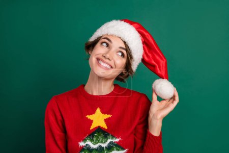 Photo of charming dreamy girl dressed ugly print pullover red cap smiling looking empty space isolated green color background.