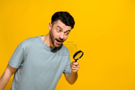 Photo of positive stylish man hold magnifying glass interested look empty space advert sale discount isolated on yellow color background.