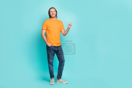 Full length photo of cheerful cute man wear orange t-shirt pointing finger empty space isolated turquoise color background.