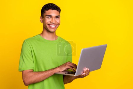 Photo de jeune attrayant beau sourire heureux homme tenir ordinateur portable programmeur facebook il développeur annonce isolé sur fond de couleur jaune.