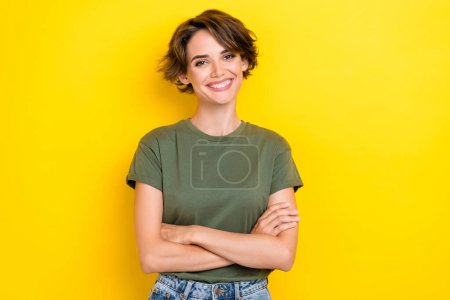 Porträt der niedlichen selbstbewussten, zufriedenen Frau mit Bob-Frisur gekleidet khaki-T-Shirt mit gefalteten Armen isoliert auf gelbem Hintergrund.
