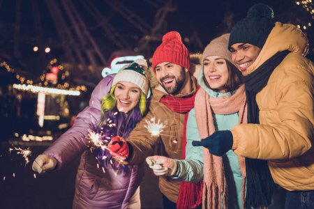 Photo of group carefree cheerful people arms hold bengal lights stick have fun advent evening outdoors.