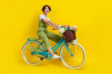 Full length photo of gorgeous young girl riding fast hurry bike traveler urban wear trendy khaki look isolated on yellow color background.