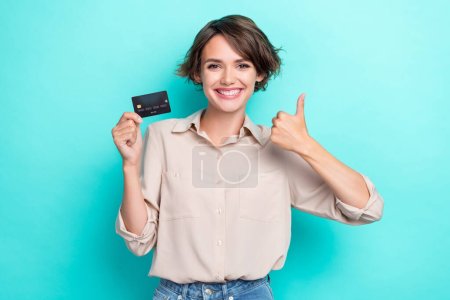 Portrait of positive optimistic girl bob hairstyle dressed beige shirt hold plastic card approve isolated on turquoise color background.