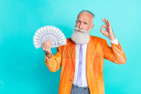 Photo de succès homme âgé confiant tenir des billets usd démontrer okey symbole isolé sur fond de couleur cyan.