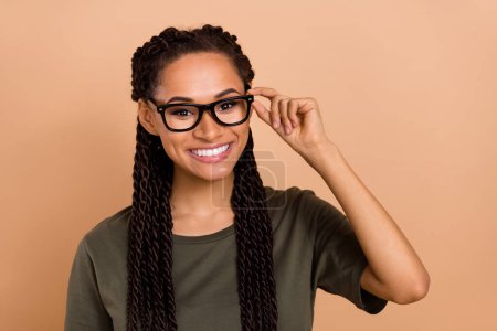 Foto von fröhlichen hübschen Mädchen zahm strahlendes Lächeln Arm Touch-Brille isoliert auf beige Hintergrund.