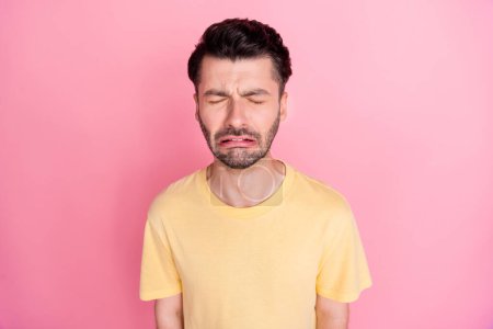 Photo of disappointed depressed unhappy guy with brunet hairstyle yellow t-shirt crying eyes closed isolated on pink color background.
