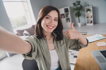 Porträt einer positiven attraktiven Sitzstuhldame mit Selfie-Zeigefinger zeigt Daumen hoch modernes Büro in Innenräumen.