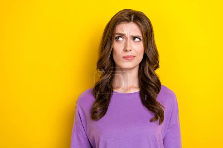 Portrait photo of young unsure minded deep think woman pouted lips look empty space dont know how app works isolated on yellow color background.