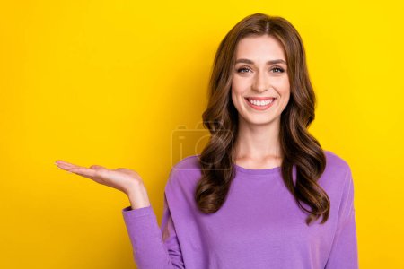 Photo of young adorable pretty lovely woman wear purple shirt hold palm empty space advertising promo isolated on yellow color background.