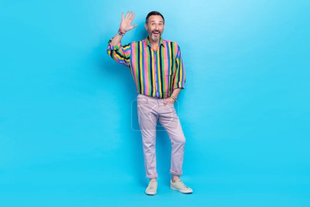 Full length photo of glamour groomed man retro trendy clothes hand pocket say hello friends colleagues isolated on blue color background.