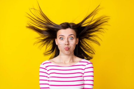 Foto-Porträt von charmanten jungen Frau aufblasen Wangen fliegen Haare töricht tragen stilvolle gestreifte Kleidung isoliert auf gelbem Hintergrund.