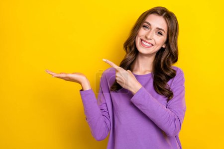 Photo of cheerful smiling woman purple jumper hold palm finger point empty space new special proposition offer isolated on yellow color background.