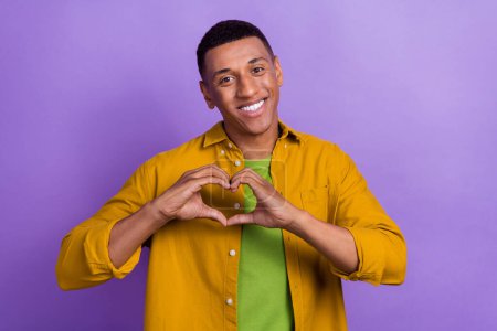 Foto-Porträt von hübschen jungen Mann zeigt Arme Finger Herzform gekleidet stilvollen gelben Kleidungsstück isoliert auf violettem Hintergrund.
