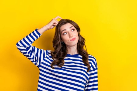 Photo of attractive young woman scratch head look interested empty space dressed stylish striped outfit isolated on yellow color background.