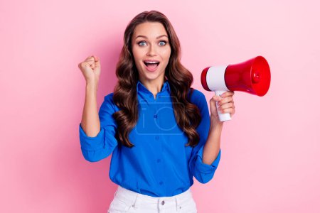 Photo of impressed ecstatic woman with curly hairdo dressed blue blouse hold megaphone clench fist isolated on pink color background.