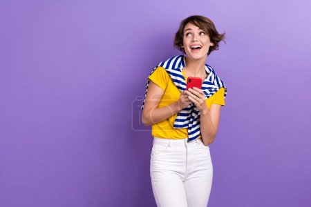 Photo of shiny dreamy woman wear tied sweater looking empty space texting modern gadget isolated purple color background.