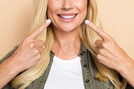 Zugeschnittenes Foto von hübschen bezaubernden Frau tragen khaki Hemd zeigt zwei Finger weiße Zähne isoliert beige Farbhintergrund.