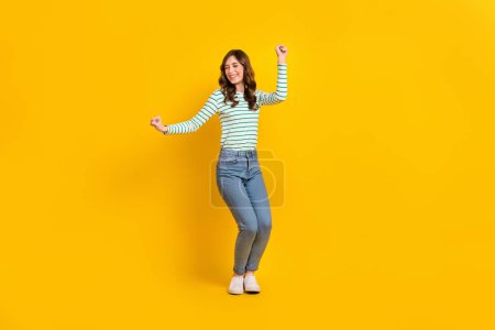 Full size photo of pleasant gorgeous woman curly hairstyle striped shirt clenching fists dancing isolated on yellow color background.