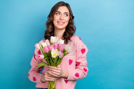 Photo of shiny thoughtful lady dressed pink cardigan holding bouquet looking emtpy space isolated blue color background.
