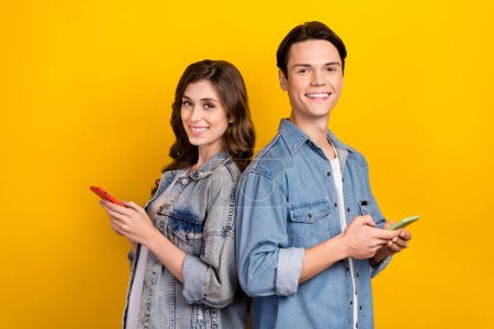 Portrait of two positive nice people hold use smart phone chatting toothy smile isolated on yellow color background. Poster 647363832