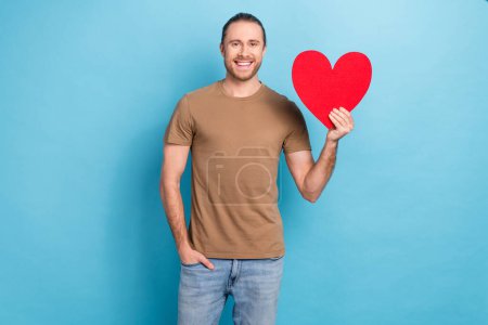 Photo advertisement banner of young smiling handsome man wear brown t-shirt holding love heart symbol sympathy isolated on blue color background. Poster 647587974