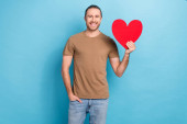 Photo advertisement banner of young smiling handsome man wear brown t-shirt holding love heart symbol sympathy isolated on blue color background. Poster #647587974