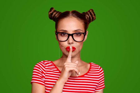 Shh Portrait of attractive mysterious girl in glasses gesturing silence sign with forefinger red pout lips looking at camera isolated on red background.