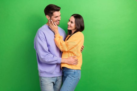 Portrait of two positive satisfied people cuddle hand touch face isolated on green color background.