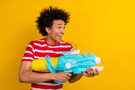 Profile photo of carefree positive person hold playing water gun look empty space isolated on yellow color background.