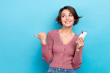 Photo of pretty dreamy woman dressed pink shirt texting modern device thumb empty space isolated blue color background.