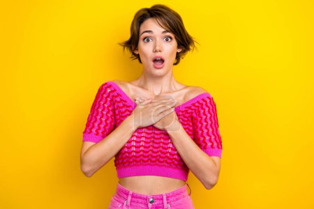 Photo of young stupor woman confused hands chest shocked wear pink knitted crop top unexpected scary movie isolated on yellow color background.