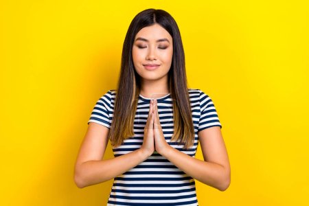 Photo picture closed eyes attractive chinese woman folded hands together chakra meditation prayer isolated on yellow color background.