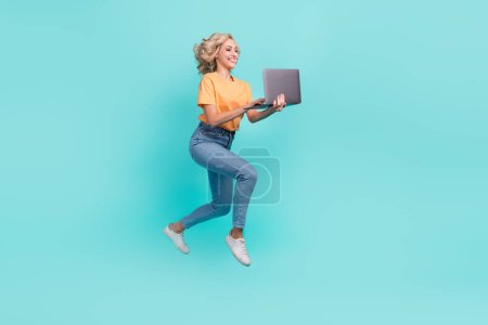 Full length photo of funky cheerful girl wear orange t-shirt jumping chatting modern device isolated turquoise color background.