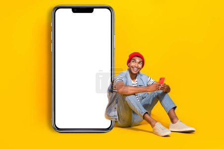 Full length photo of pretty dreamy guy dressed denim clothes chatting gadget empty space isolated yellow color background.