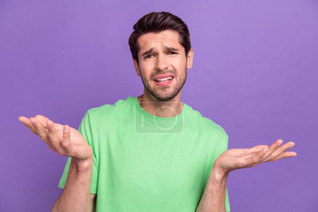 Photo of funny young guy shrug shoulders wearing green t-shirt dissatisfied misunderstanding dude chill isolated on violet background.