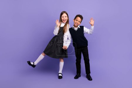 Photo of positive schoolkids have fun on school first day waving hands isolated bright color background.