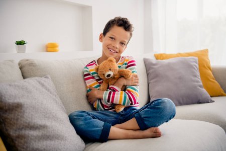 Photo of cute adorable kid homeschool stay home quarantine embrace teddy bear play on couch indoors.