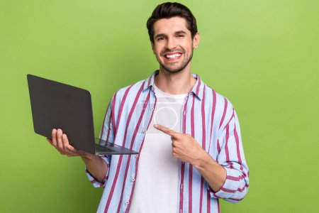 Portrait of young positive man indicate finger empty space laptop high efficiency new technologies isolated on green color background.