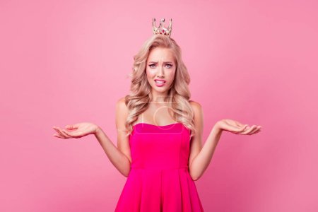 Portrait of confused questioned girl raise hands say tell wear crown head isolated on pink color background.