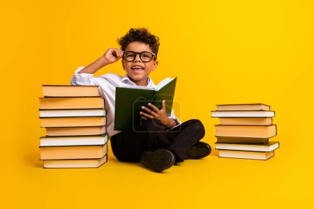 Full body photo of little positive diligent schoolkid sit floor read pile stack book prepare text isolated on yellow color background.