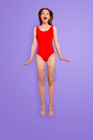 Full-body vertical portrait of happy girl in a red swimsuit with bright lipstick on her lips happily screams jumping over the air isolated on yellow background.