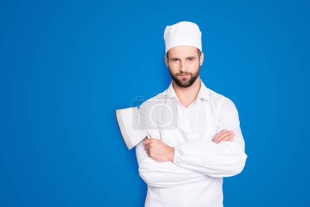 Portrait of handsome attractive butcher in beret having his arms crossed holding metal cleaver looking at camera isolated on grey background.