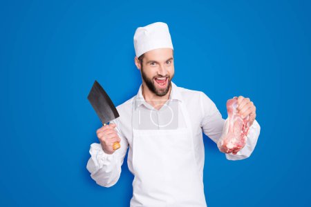 Portrait of crazy funny butcher with stubble having cleaver and fresh meat in arms, shouting, screaming with open mouth, isolated on grey background.