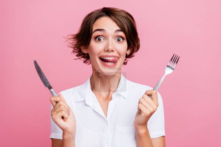 Photo of pretty charming toothy girl licks her teeth she is hungry waiting eating using fork and knife isolated on pink color background.