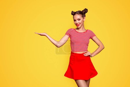 Werbekonzept empfehlen. Porträt der jungen netten brünetten Dame hält und demonstriert unsichtbares Produkt auf der Hand isoliert auf rotem Hintergrund mit Kopierraum.