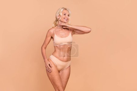 Photo of charming lovely lady dressed trendy bra panties touch face chin look empty space isolated on beige color background.