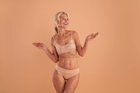 Photo of pretty excited middle age woman wear bikini rising hands arms looking empty space isolated beige color background.