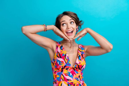 Photo of impressed nice woman with bob hair dressed colorful clothes look empty space arms on face isolated on blue color background.